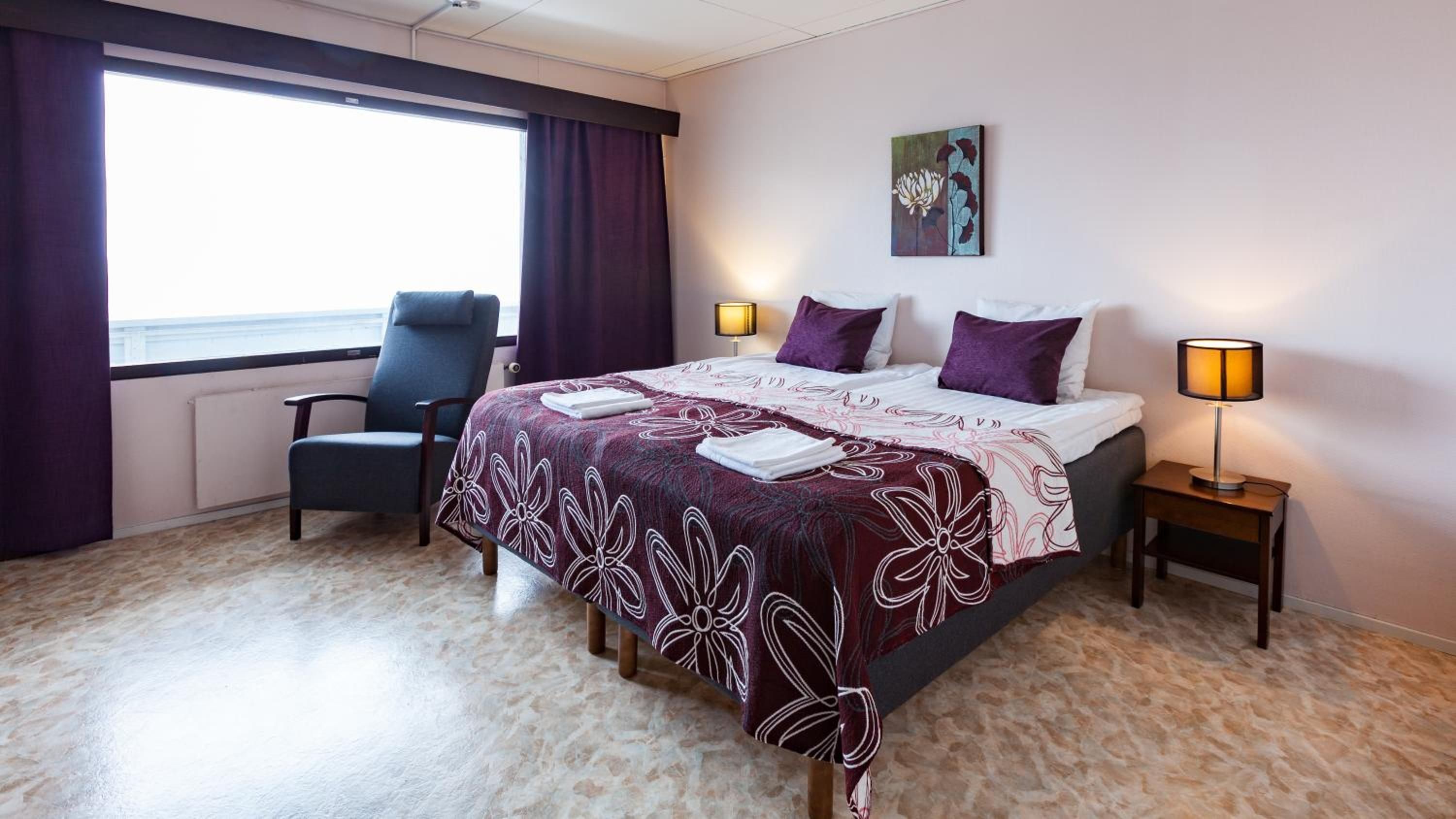 Una habitación de hotel con una cama, una silla, una lámpara y un cuadro en la pared.