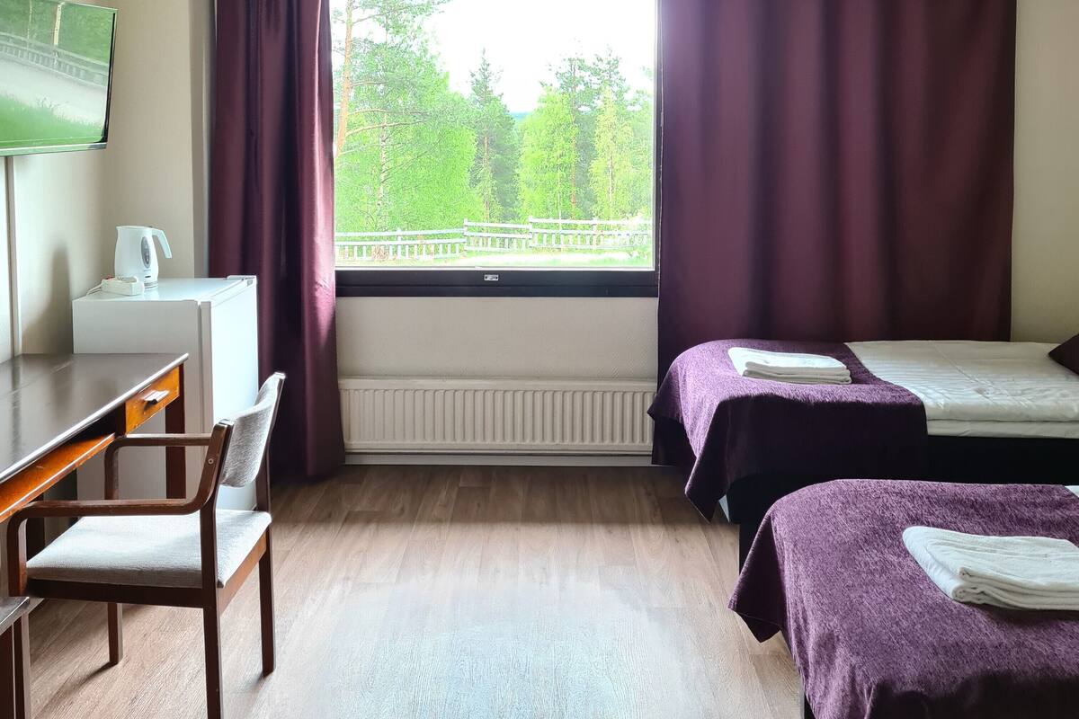 A hotel room with a desk, two beds, a TV, and a window with curtains.