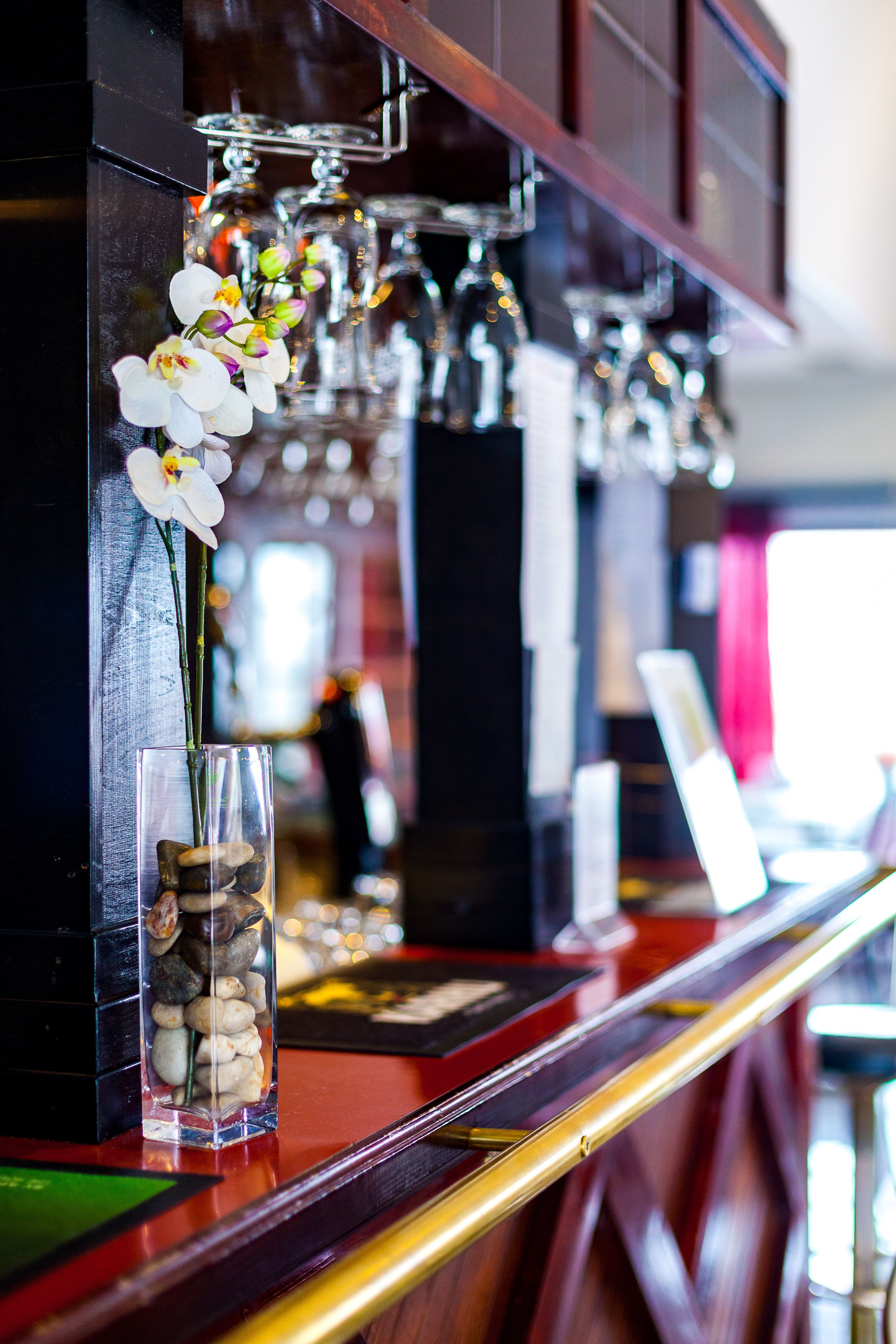 Zona de bar con un jarrón de cristal transparente que contiene orquídeas blancas y un arreglo de piedras pequeñas.