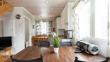 Een moderne keuken met witte kasten, een eethoek met een houten tafel en stoelen, en een groot raam met gordijnen.