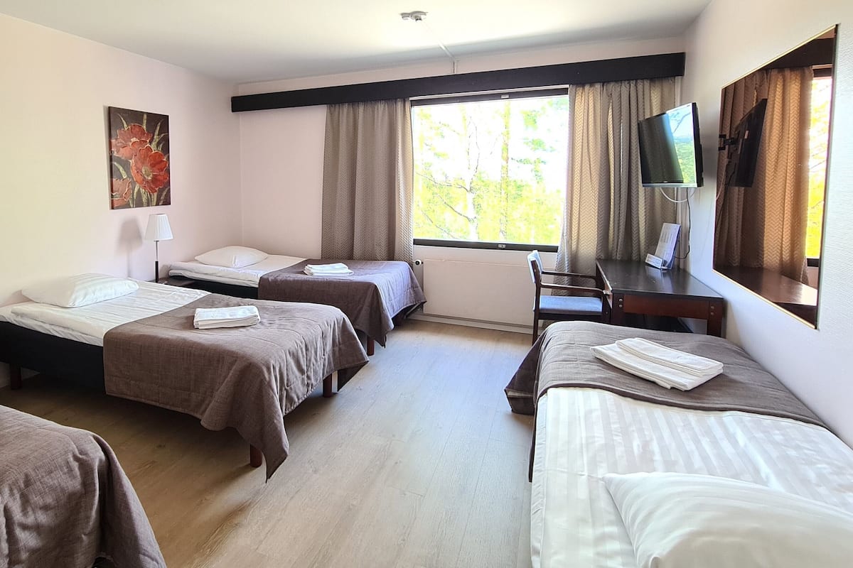 A hotel room with two single beds, a desk with a chair, a TV, and a window with curtains.