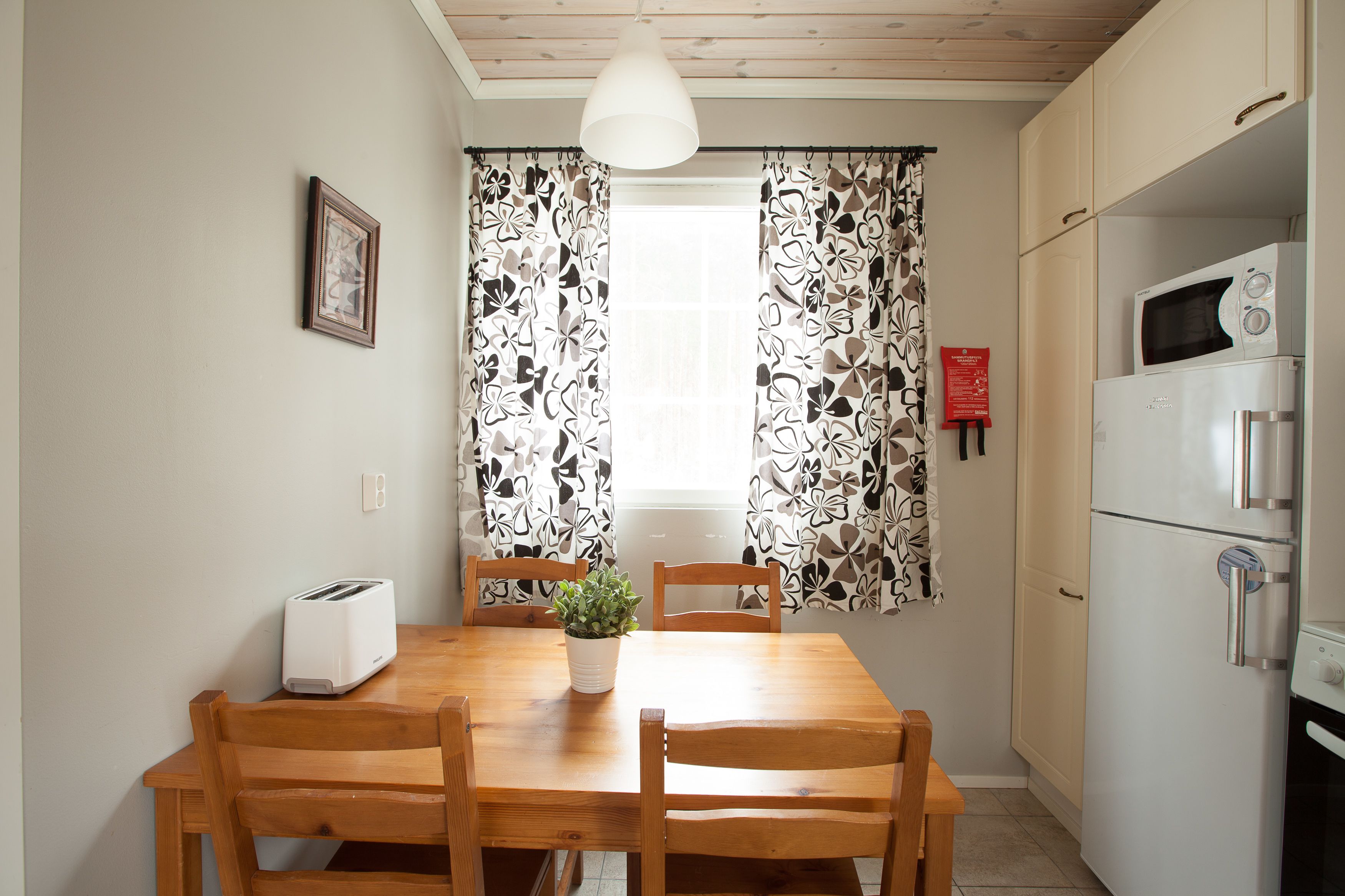 Una cocina compacta con una mesa de comedor, sillas, un tostador, un microondas y un refrigerador.