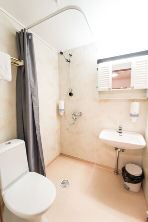 A bathroom with a toilet, sink, shower, and a window with shutters.