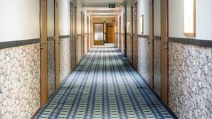 A hotel hallway with patterned carpet, wooden doors, and a tiled wall.