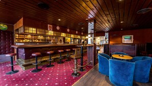 A bar area with a wooden ceiling, red carpet, stools, and blue upholstered chairs.
