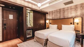 Habitación de hotel con dos camas, un armario de madera, un espejo y una mesita de noche con lámpara.