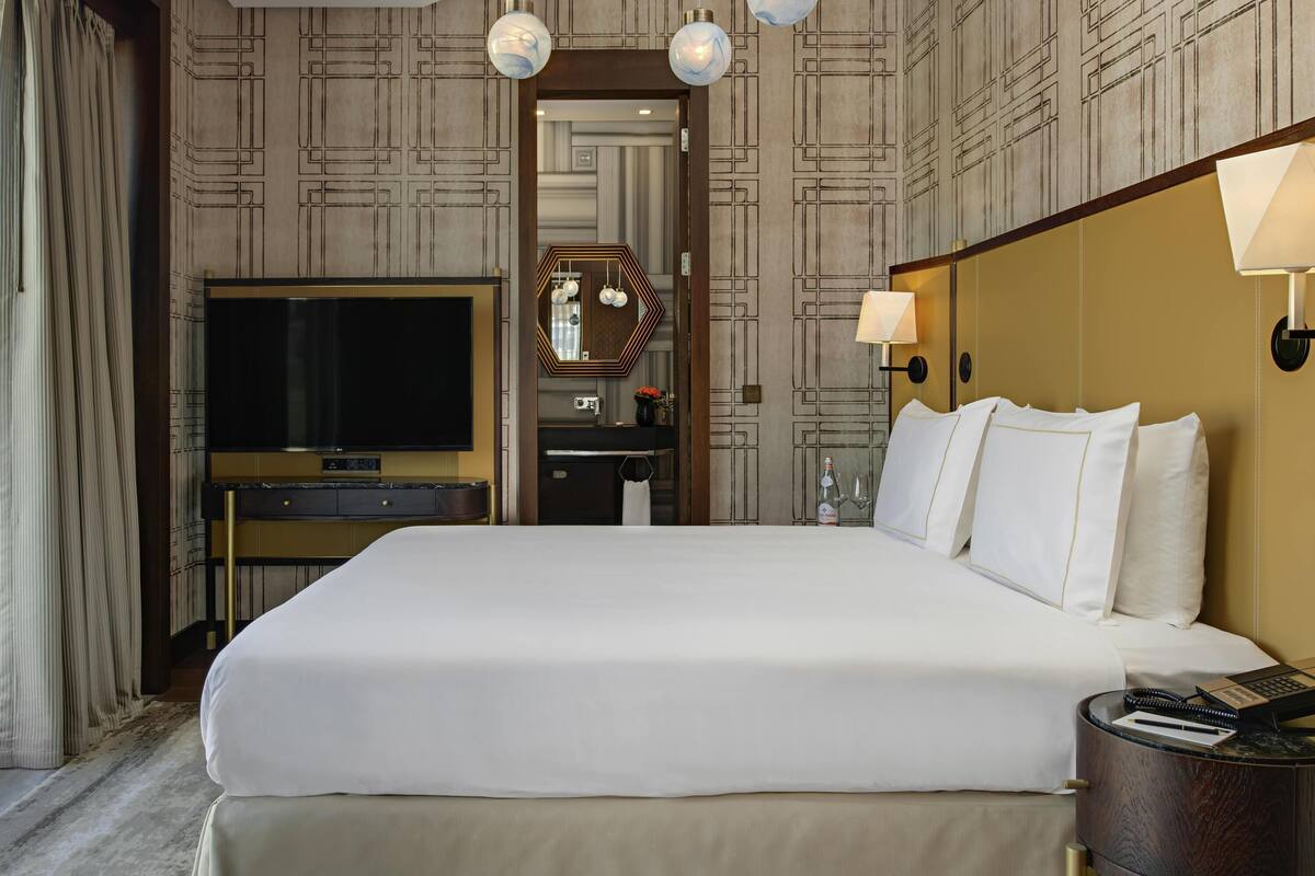 Ein Hotelzimmer mit einem großen Bett, einem Fernseher, einer Minibar und einem durch eine geöffnete Tür einsehbaren Badezimmer.