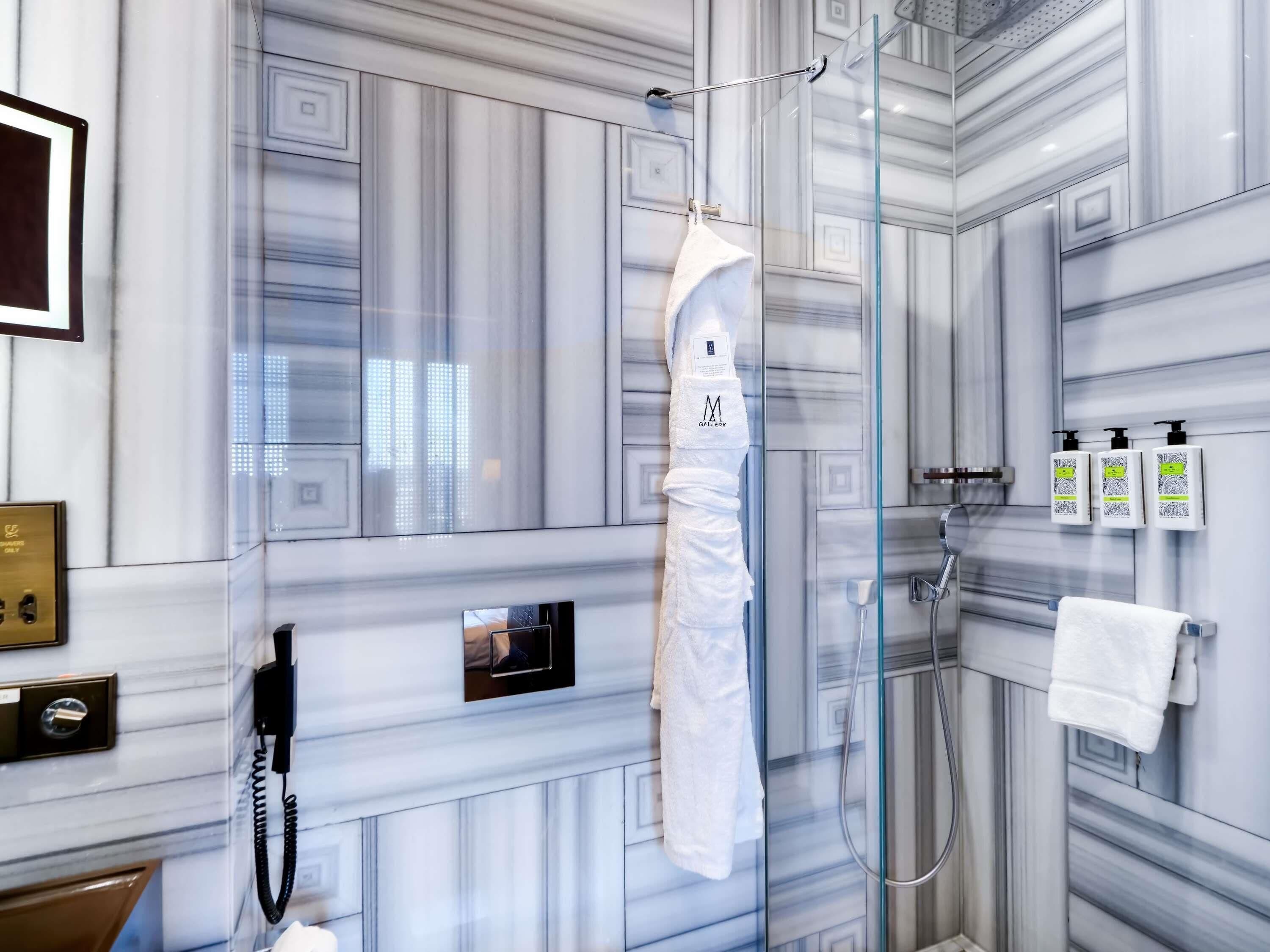 A modern bathroom with a glass shower enclosure, a towel rack with a white towel, a phone, and toiletries on the wall.