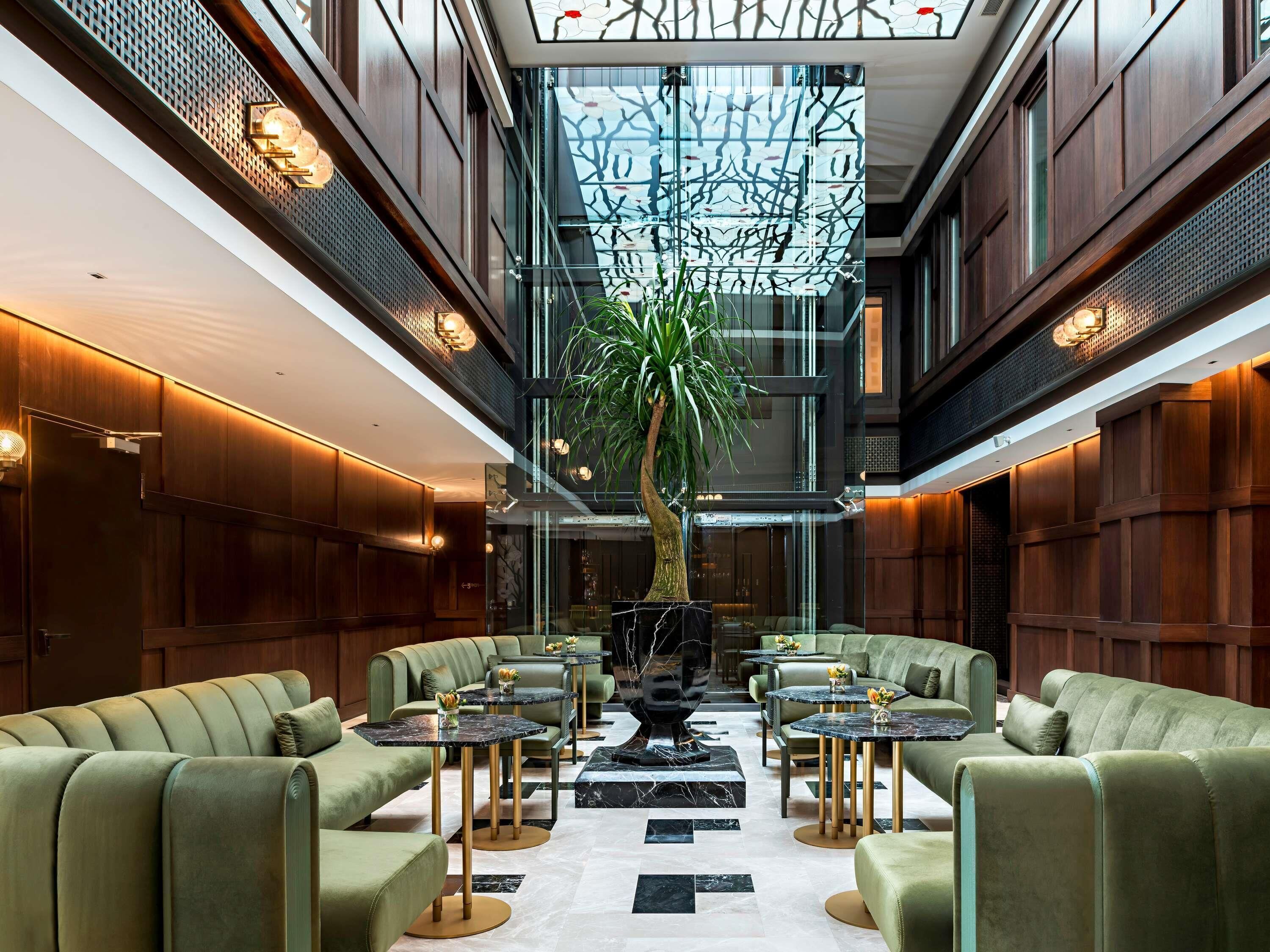 A spacious lobby with high ceilings, a central tree, and multiple seating areas.