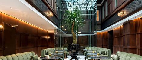 A spacious lobby with high ceilings, a central tree, and multiple seating areas.