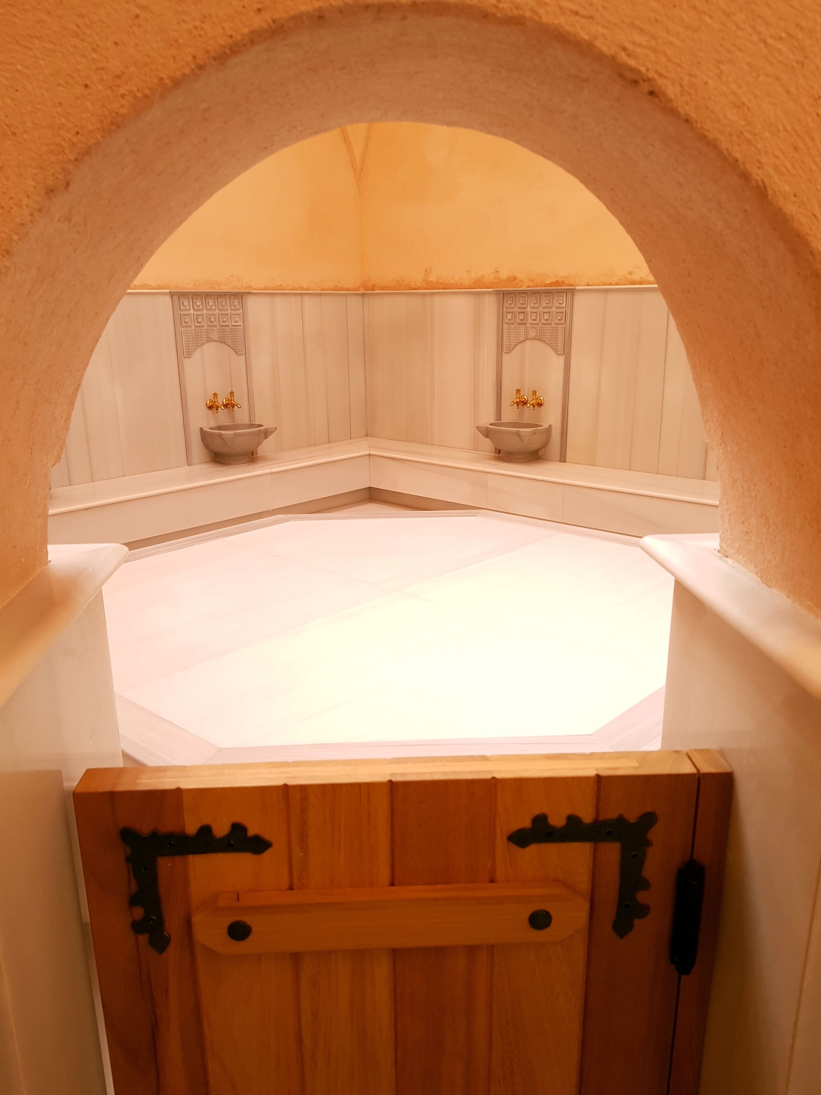 A spa room with a large octagonal hot tub, two sinks with gold faucets, and a wooden door with metal handles.