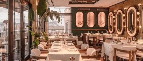 A restaurant with tables set for dining, large windows, and a city view.
