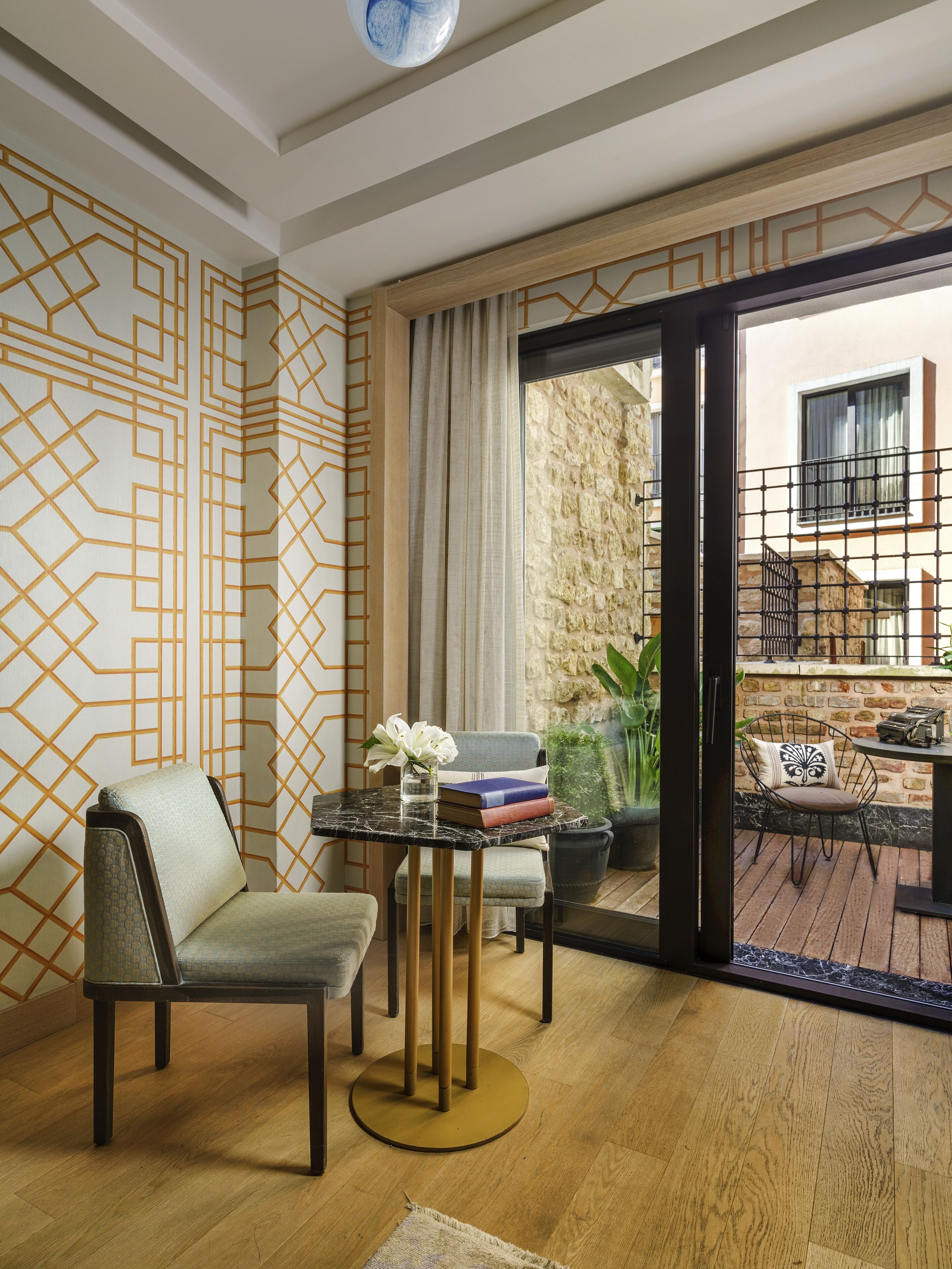 Una sala moderna con un sofá, una mesita redonda con libros y un florero, y vistas a un patio exterior.