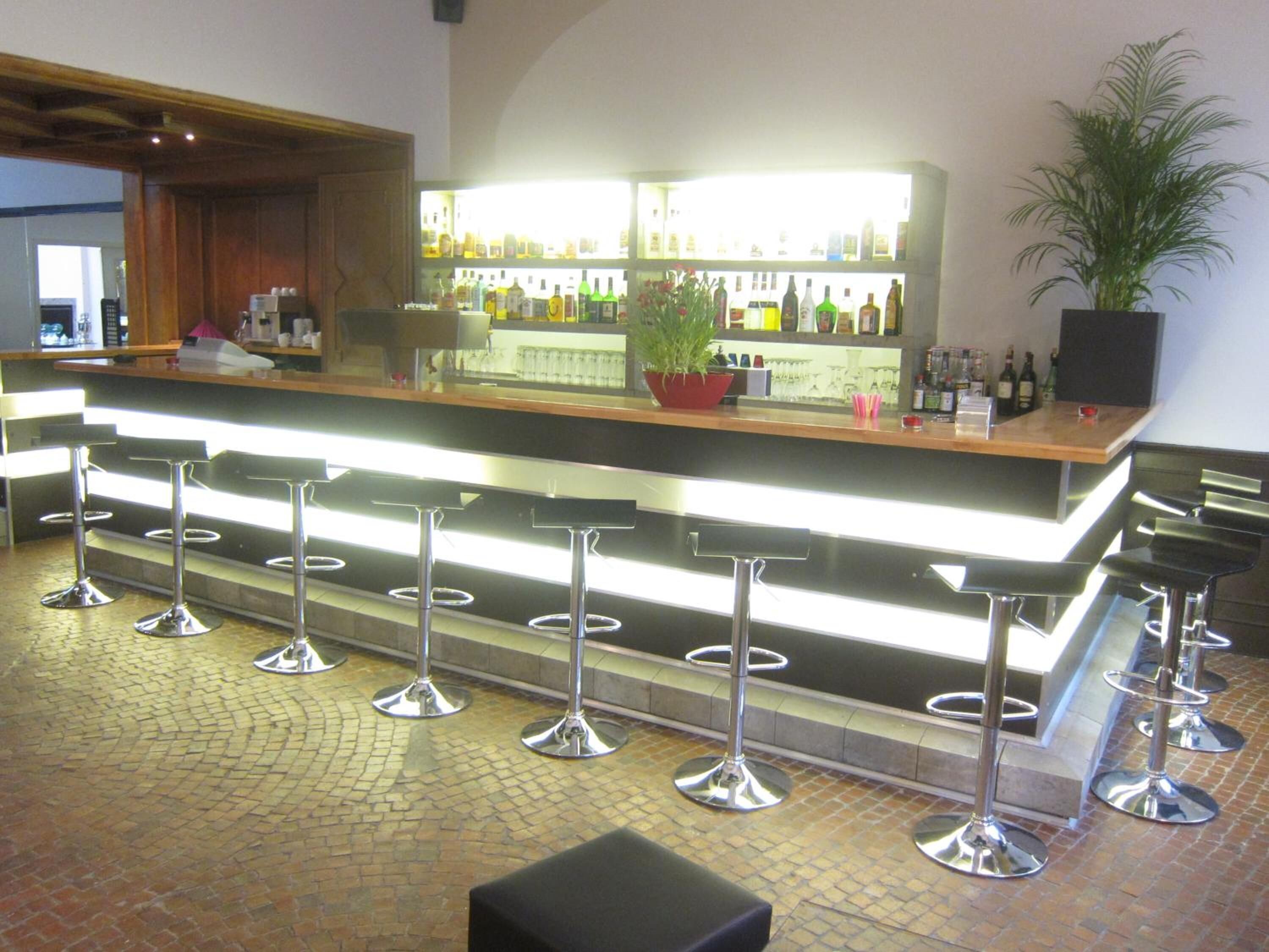 Una zona de bar con mostrador, taburetes y una planta en maceta.