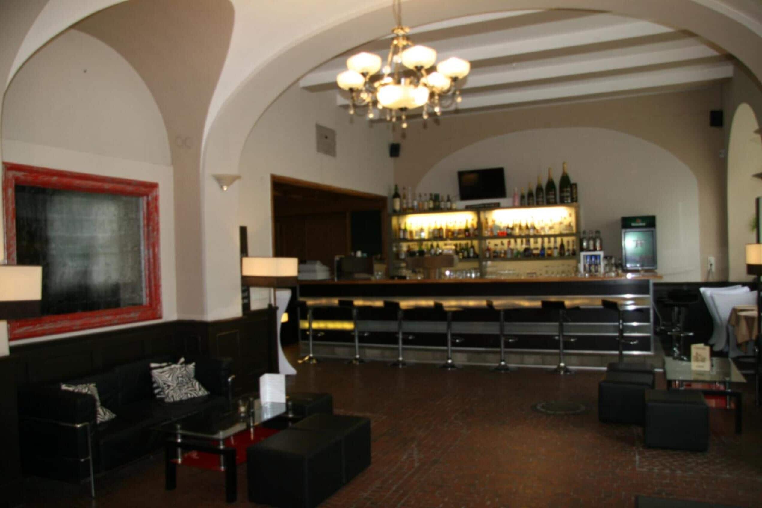 A bar area with a long counter, shelves with bottles, and a television screen.