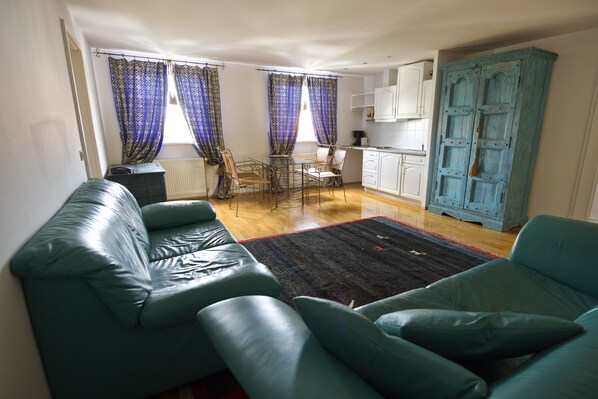 Una sala de estar con un sofá, una mesa de comedor con sillas, una zona de cocina y un armario azul.