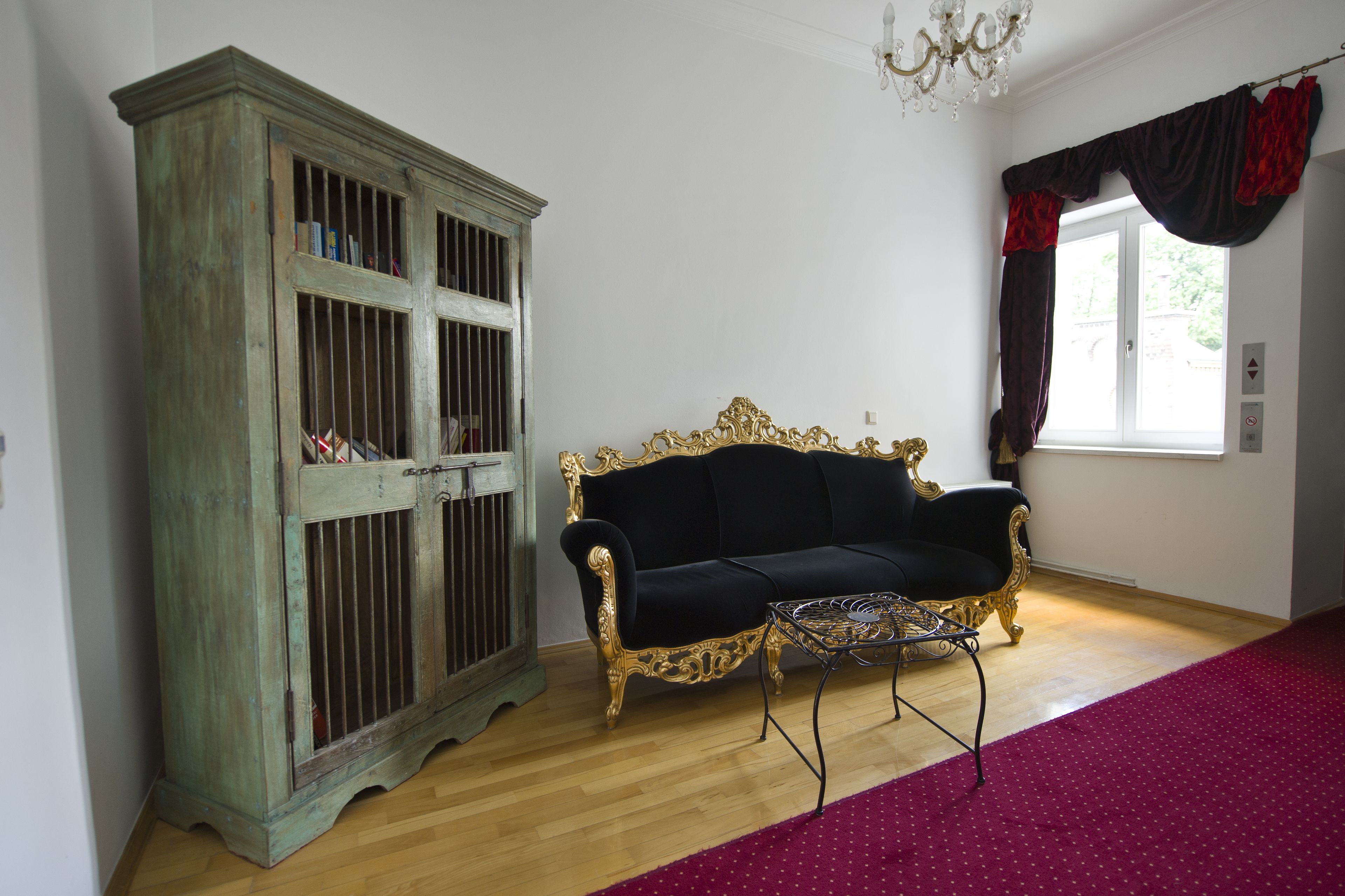 Una habitación con un aparador verde antiguo, un sofá tapizado negro y una alfombra roja estampada.