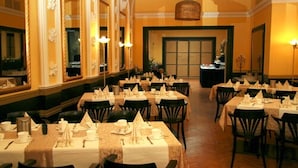 Un comedor formal con varias mesas dispuestas para el servicio, grandes espejos y candelabros.