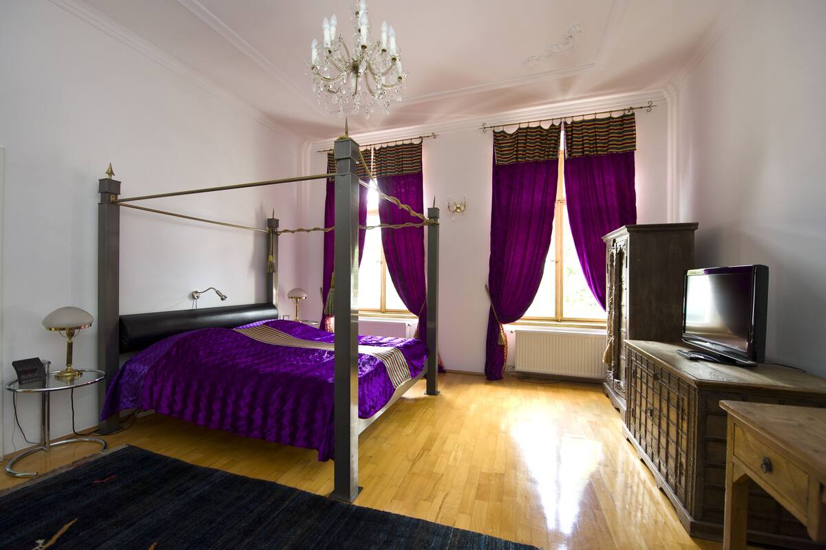 Une chambre à coucher avec un lit à baldaquin, un téléviseur posé sur une commode en bois et un lustre.