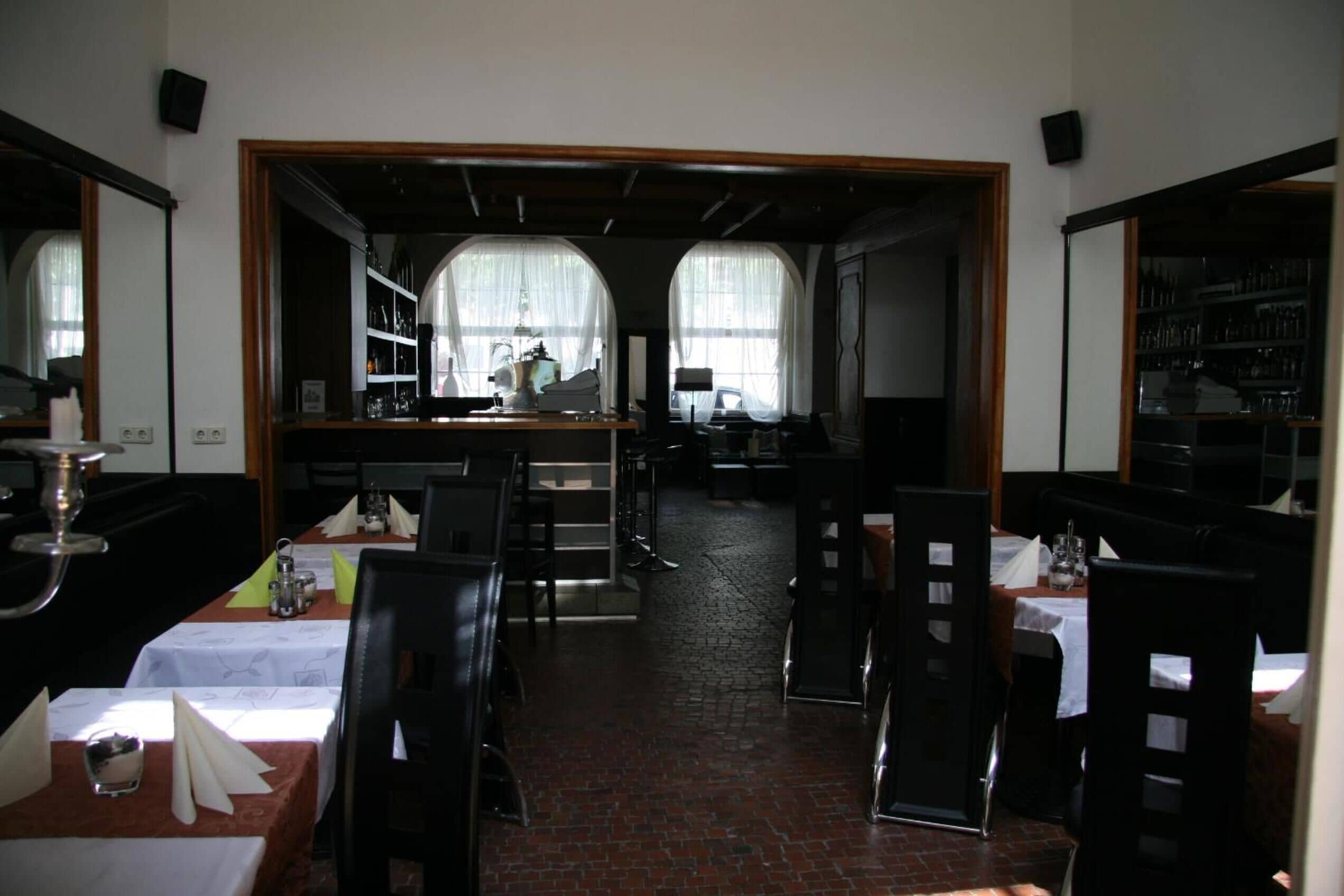 Ein Restaurant mit gedeckten Tischen, einer Bar und Blick durch große Fenster.