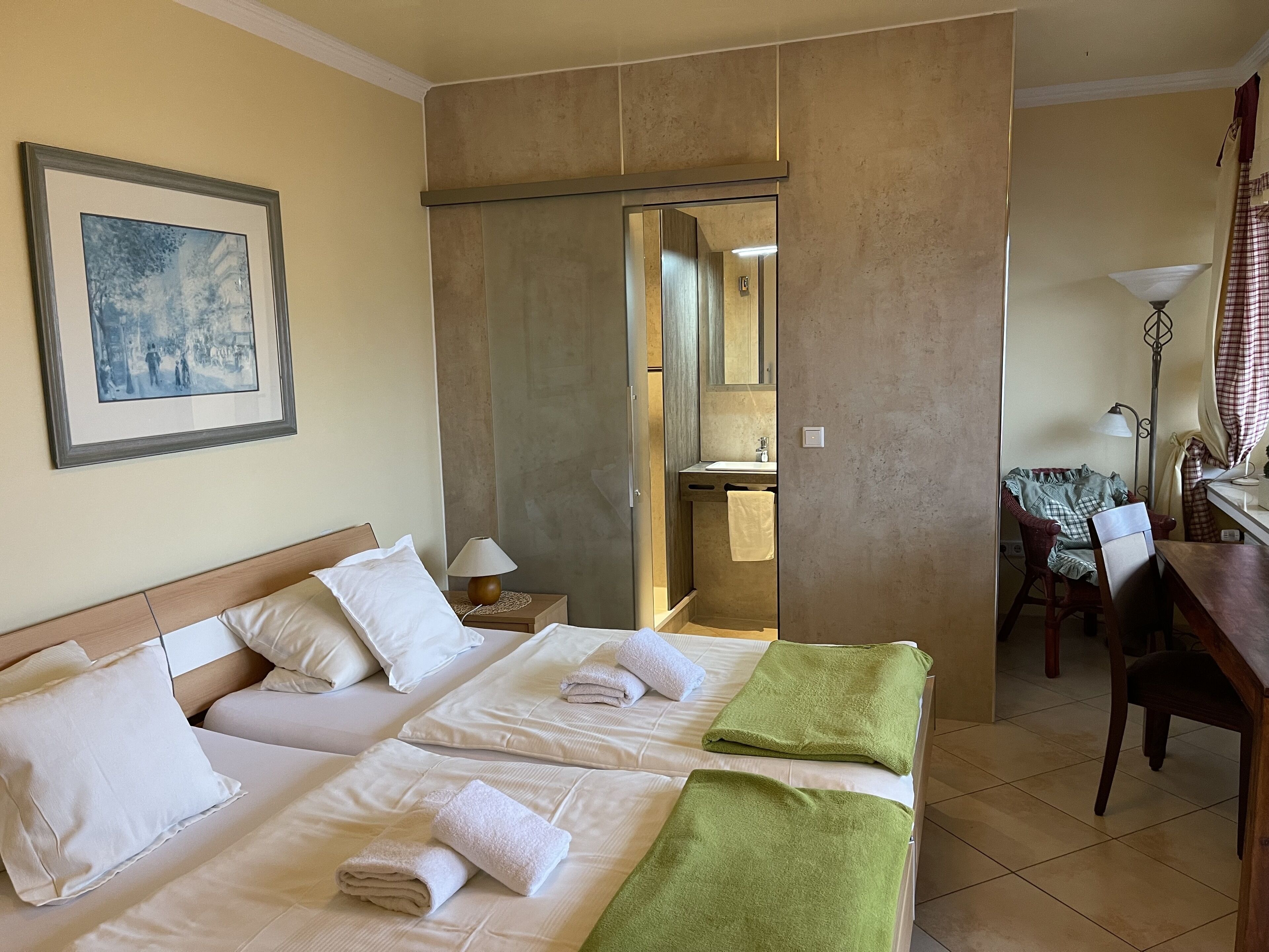 Une chambre d’hôtel avec deux lits, un bureau, une chaise, un miroir et un tableau encadré au mur.