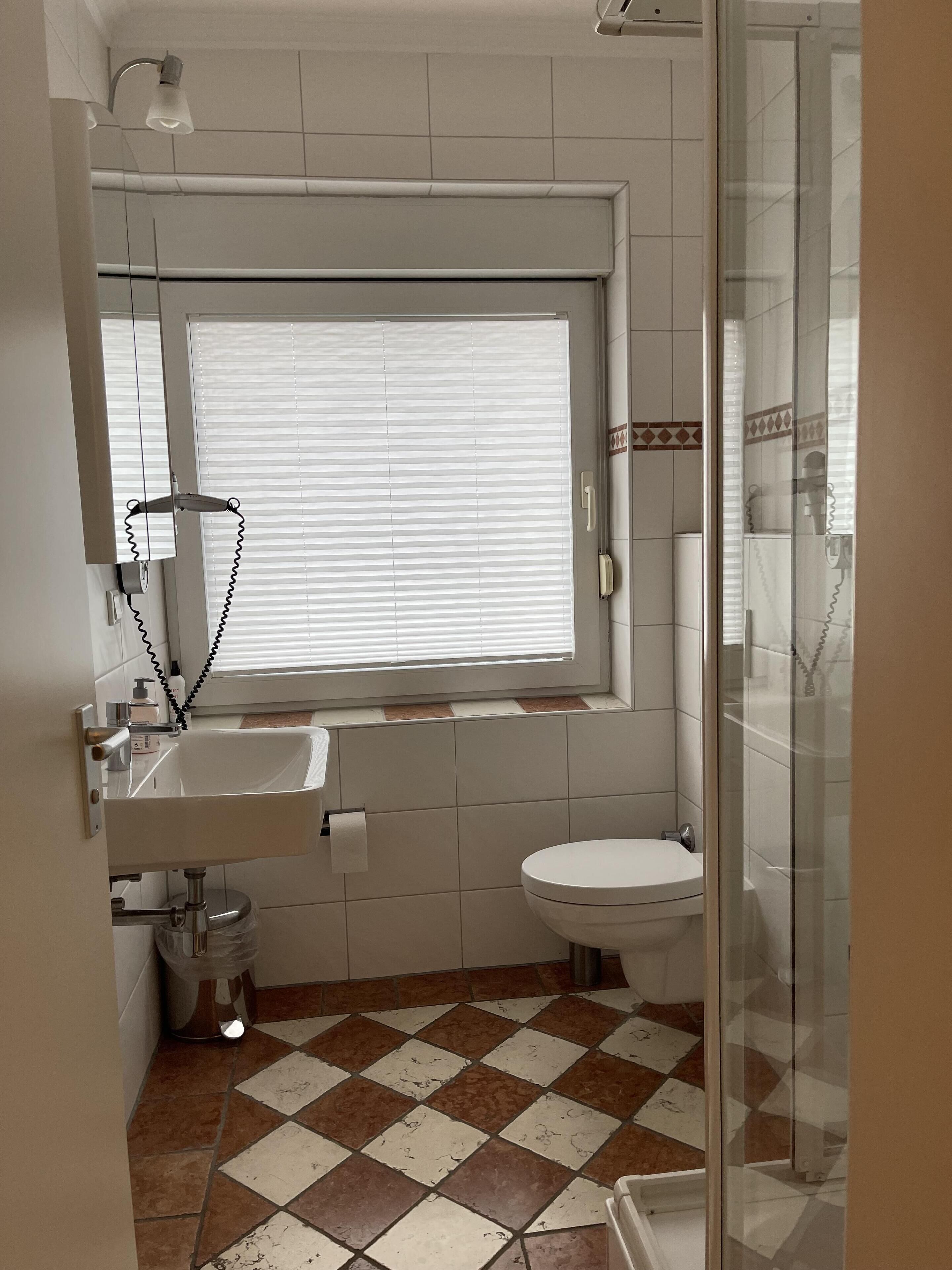 Et lille badeværelse med vindue, vask, toilet og brusebad.