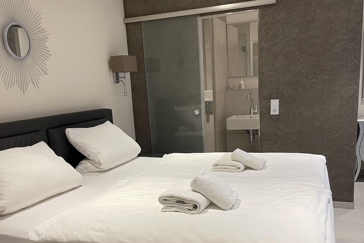 A modern hotel room with a large bed, a glass shower door, and a mirror on the wall.