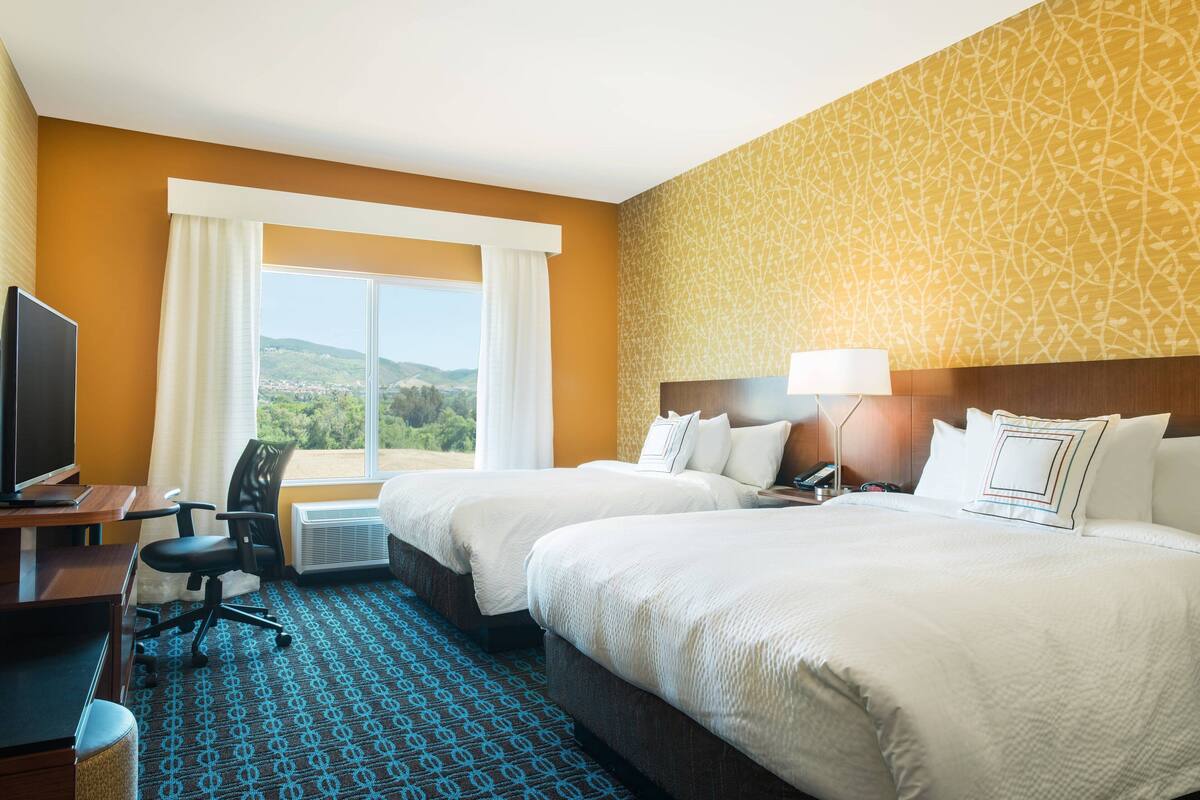 Habitación de hotel con dos camas, un escritorio, una silla, un televisor y vistas al exterior.