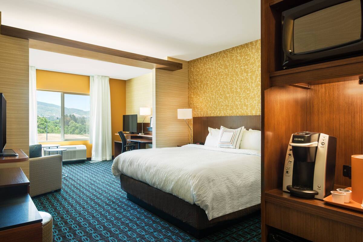 Una habitación de hotel con una cama grande, un escritorio con silla, televisión y cafetera.