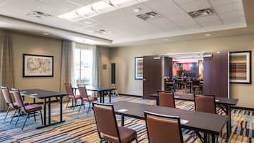 A conference room with a large table and chairs, a carpeted floor, and a view of the dining area.