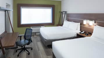 A hotel room with a desk, two beds, a chair, a window, and a nightstand with a phone and lamp.