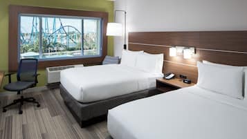 Habitación de hotel con dos camas, un escritorio, una silla, un ventanal con vistas a un parque temático y una mesita de noche con un teléfono y un reloj.