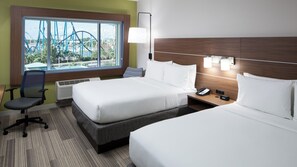 A hotel room with two beds, a desk, a chair, a window with a view of a theme park, and a bedside table with a phone and a clock. - Holiday Inn Express & Suites Orlando at SeaWorld by IHG (Orlando)