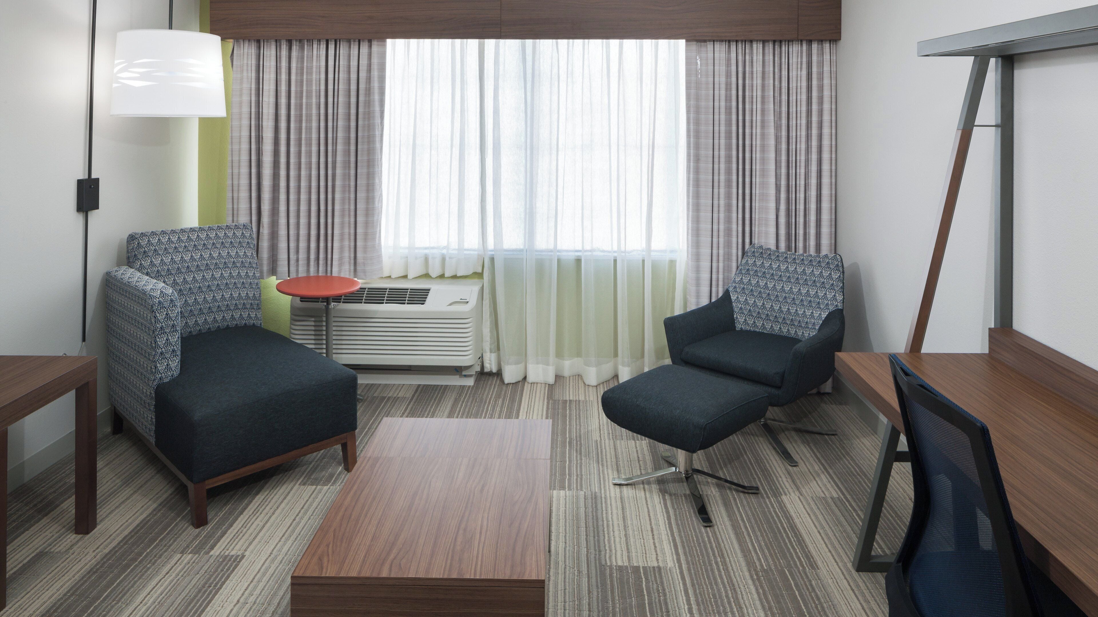 Een hotelkamer met twee fauteuils, een tafeltje, een televisie en een raam met gordijnen.
