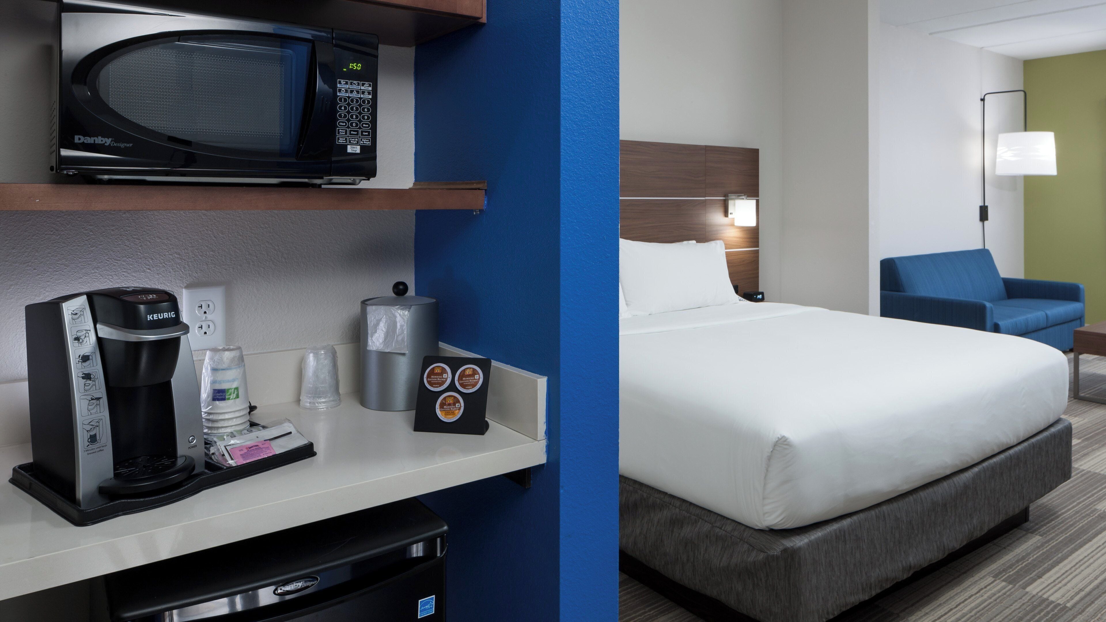 A hotel room with a bed, a coffee machine, a microwave, and a minibar.