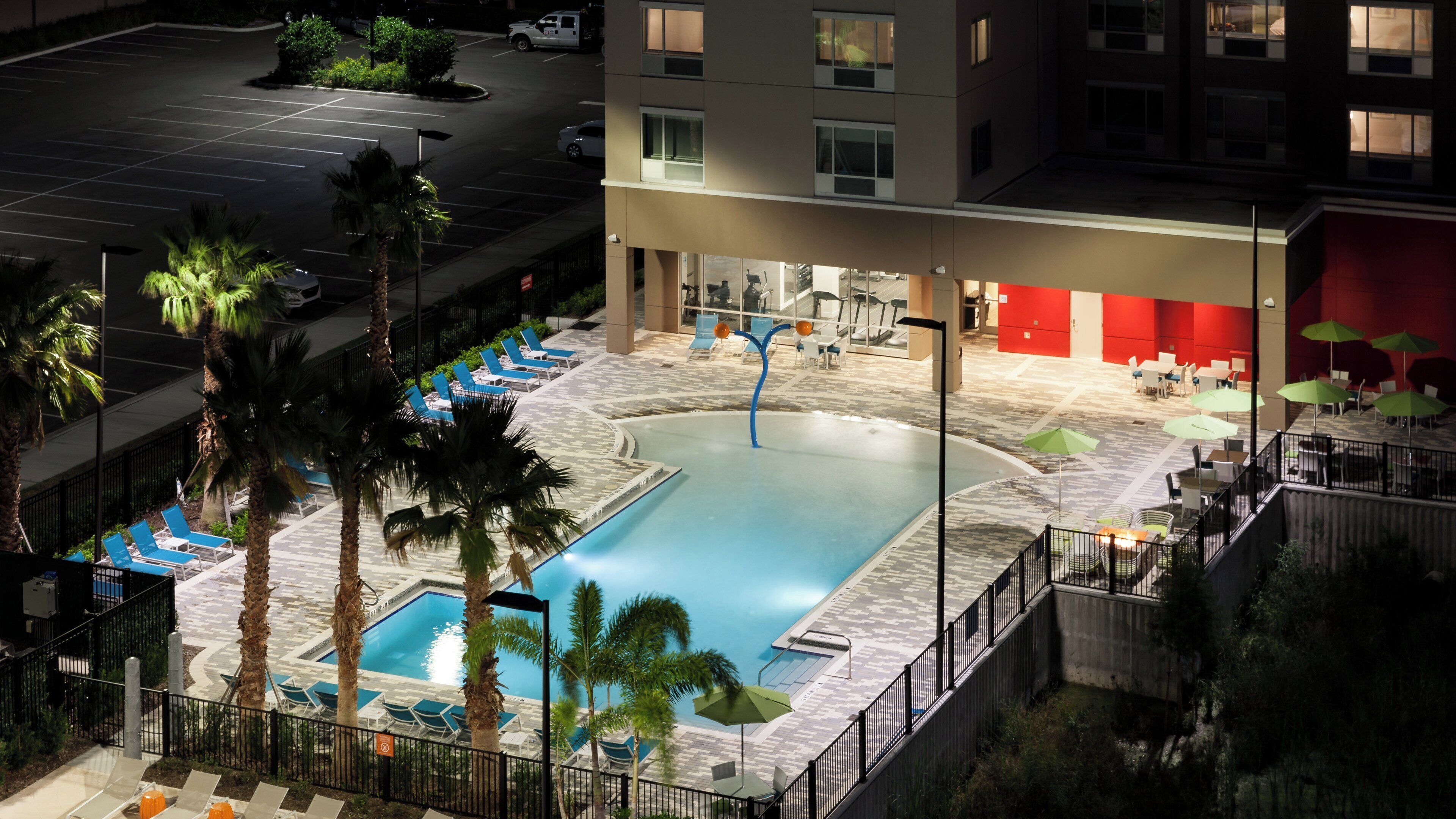 A hotel with a swimming pool surrounded by lounge chairs and palm trees.