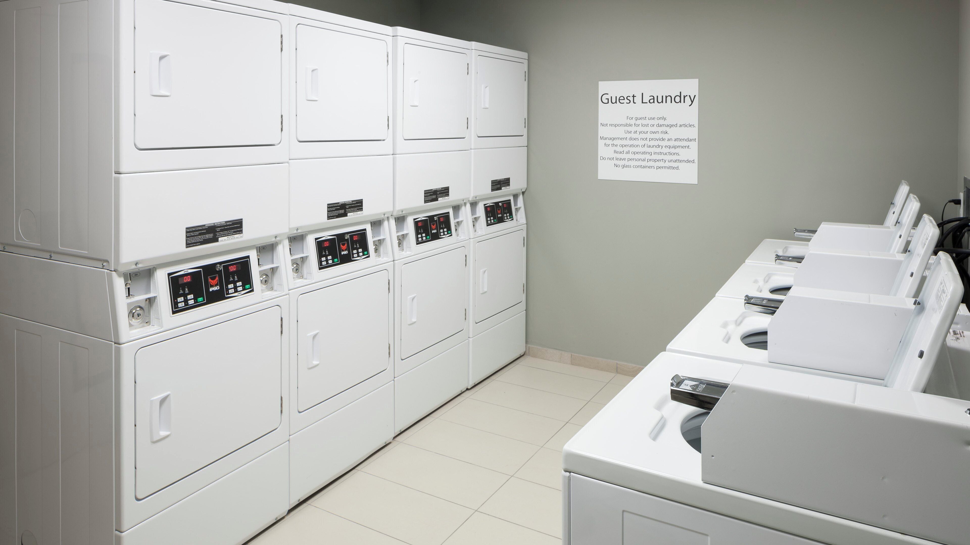 A laundry facility with multiple washing machines and dryers, a sign indicating guest use, and a tiled floor.