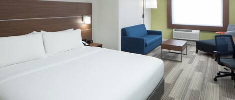 Una habitación de hotel con una cama grande, un sillón azul, una mesita pequeña y un escritorio con una silla.