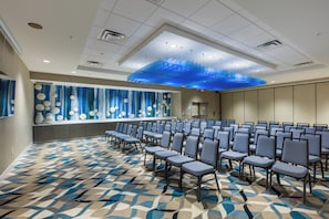 A conference room with rows of chairs, a patterned carpet, and a blue decorative ceiling feature. - Holiday Inn Express & Suites Orlando at SeaWorld by IHG (Orlando)