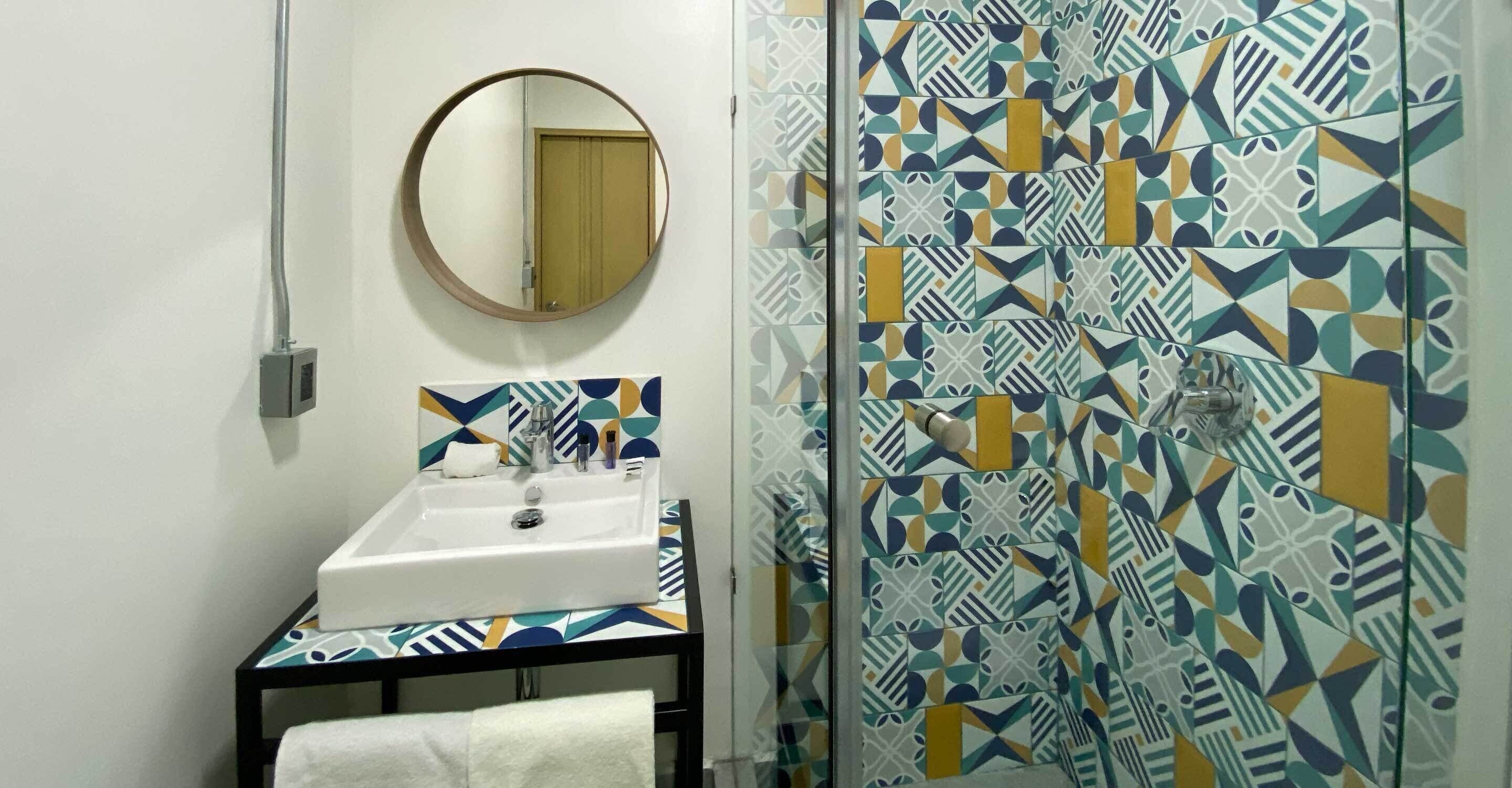 A bathroom with a white sink, a mirror, and a patterned shower wall.