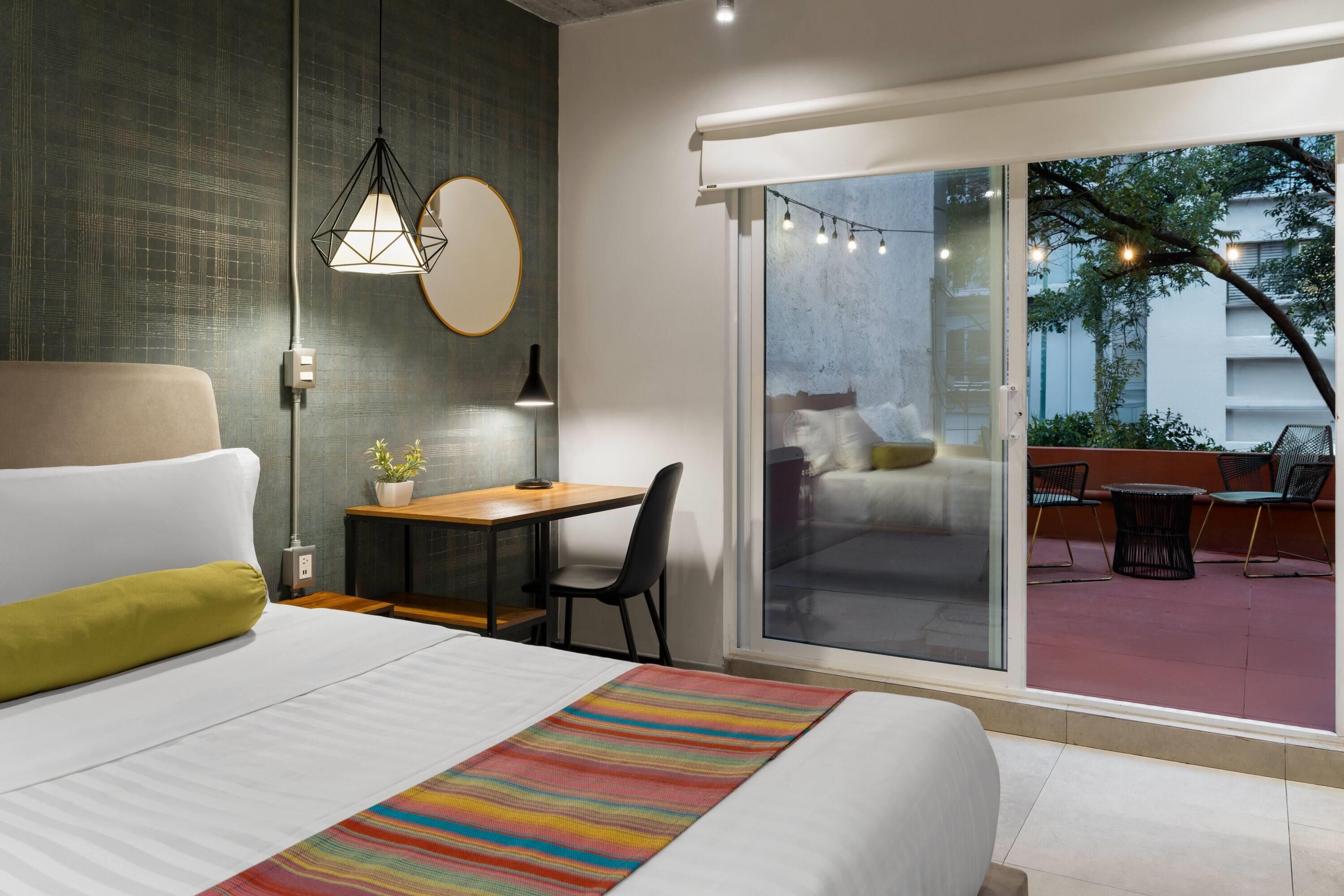 Una habitación de hotel moderna con cama, escritorio y vista al área exterior.