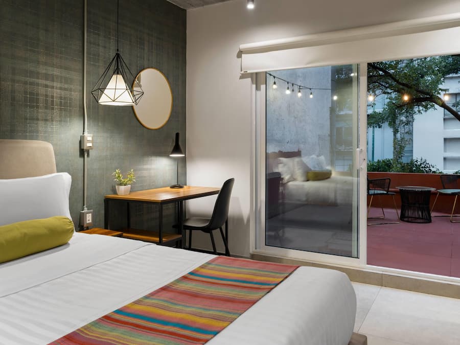 A modern hotel room with a bed, a desk, and a view of the outdoor area.