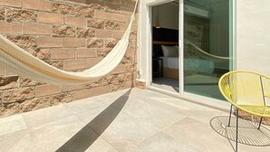 A hammock tied to a brick wall, a yellow chair, and a sliding glass door leading to a bedroom with a bed and a nightstand. - Hotel VIVE MX wtc CDMX, Trademark Collection by Wyndham (Mexico City)