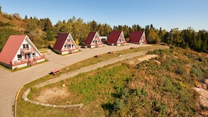A row of three red-roofed cabins with balconies, set on a sloped terrain with a dirt path leading to them. - Chalets de l'anse a Jos et anse a Yves (Essipit)