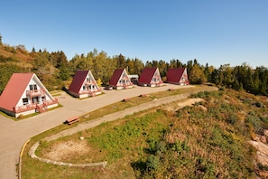 Eine Reihe von drei Holzhütten mit roten Dächern und Balkonen, gelegen in einer Hanglage mit einem Feldweg, der zu ihnen führt.