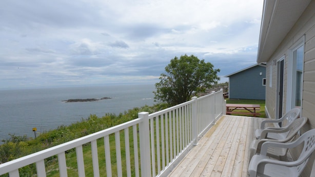 A wooden deck with white railings overlooking a body of water, a picnic table, and a small shed. - Chalets de l'anse a Jos et anse a Yves (Essipit)