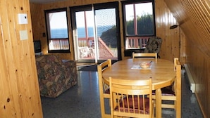 A wooden interior with a dining table, chairs, a patterned sofa, and large windows offering a view of the outdoors. - Chalets de l'anse a Jos et anse a Yves (Essipit)