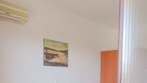 Une chambre d’hôtel avec un lit simple, une table de chevet avec une lampe, un tableau au mur et un appareil de climatisation.