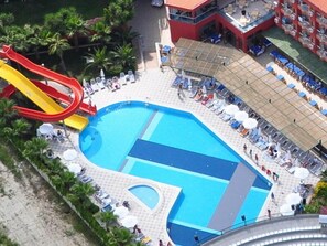 Ein großer Außenpool mit roter Rutsche, umgeben von Liegestühlen und Sonnenschirmen.