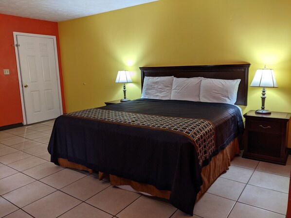 A hotel room with a bed, two bedside lamps, a nightstand, and a door. - Reelfoot Lake Inn (Tiptonville)
